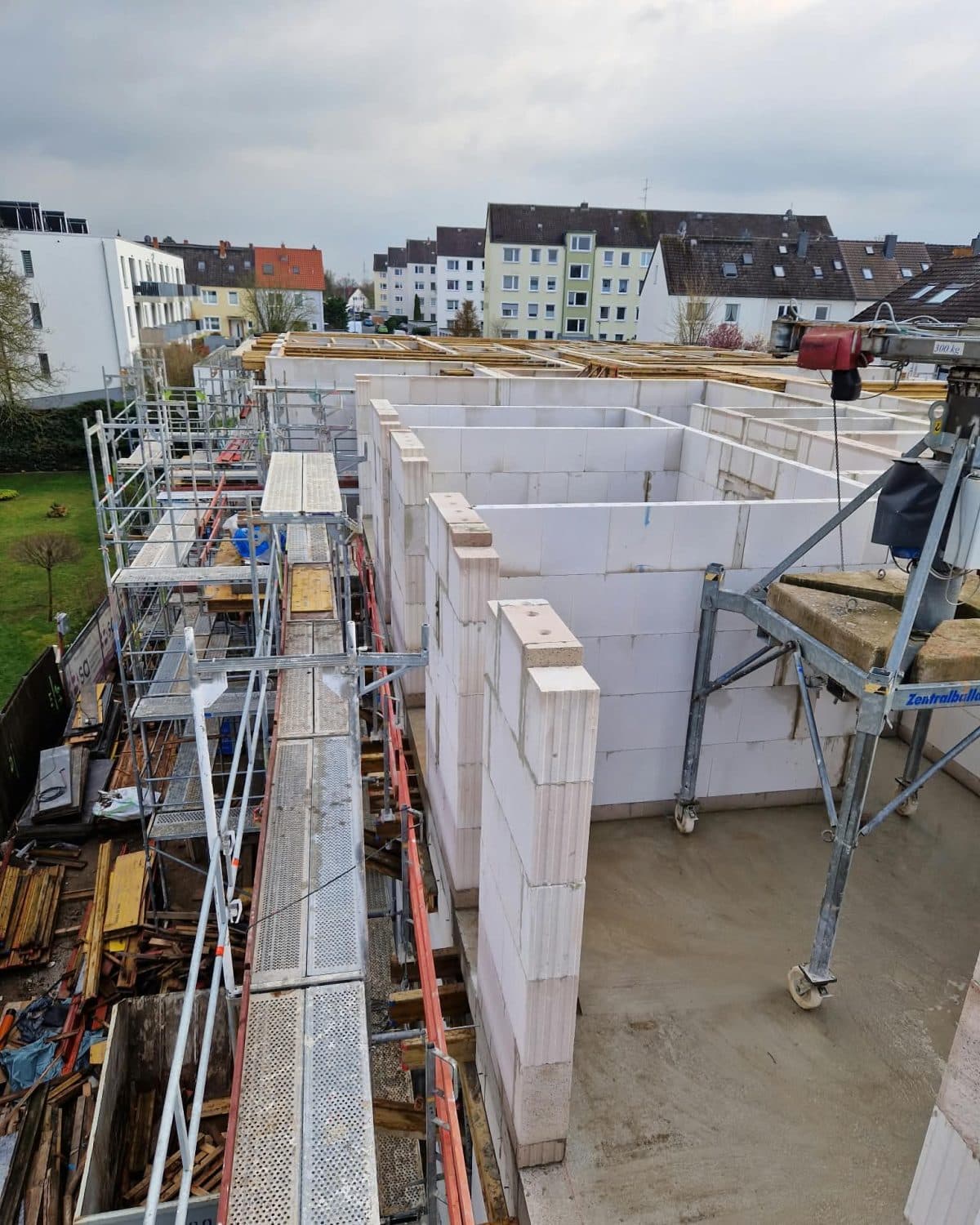 Mehrfamilienhaus im Rohbau vom Gerüst aus: Kalksandsteinwände des Obergeschosses, rechts das Versetzgerät, im Hintergrund die Nachbarhäuser