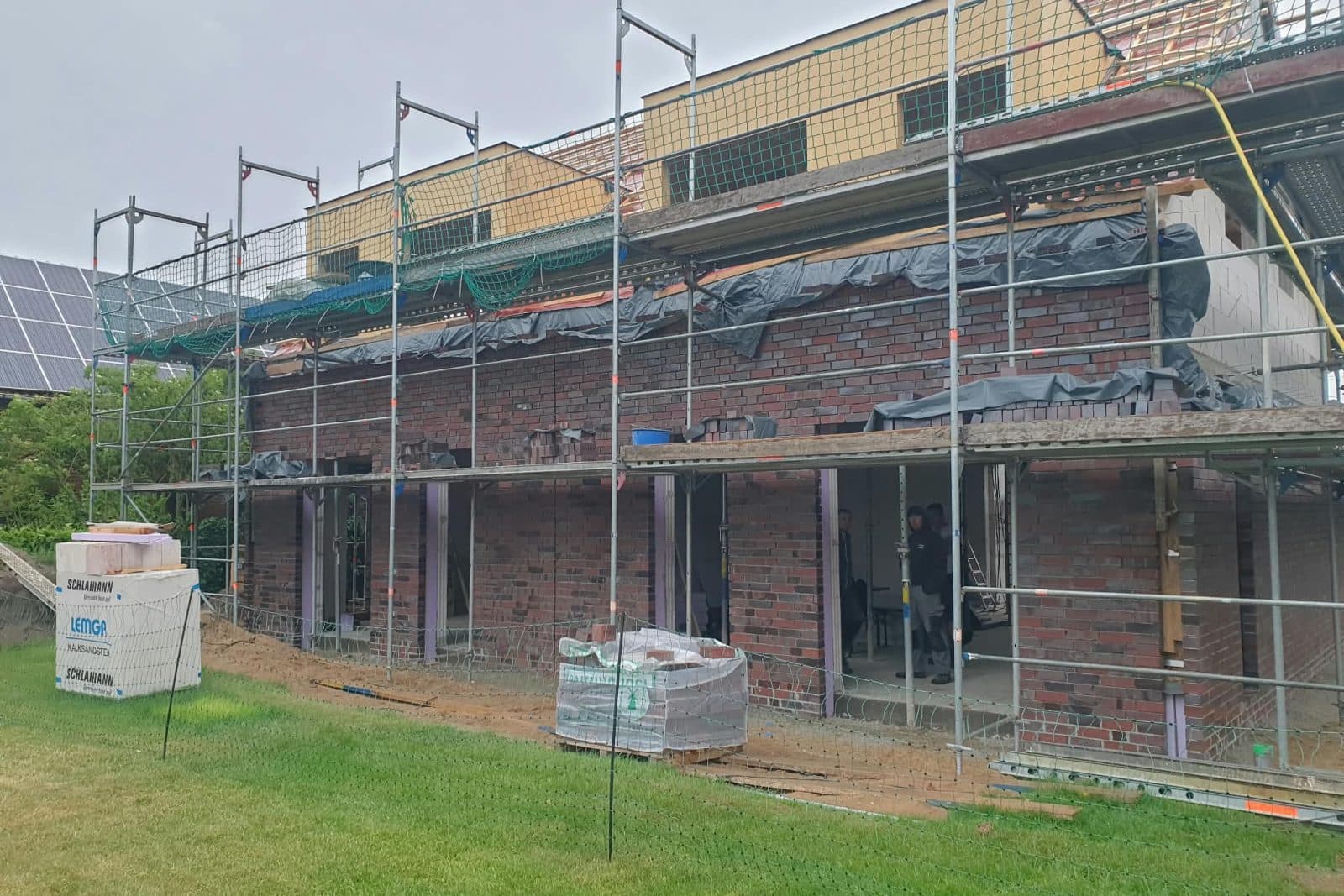 Mehrfamilienhaus mit dunkelroter Klinkerfassade, eingerüstet, im Dachgeschoss noch die Dämmung